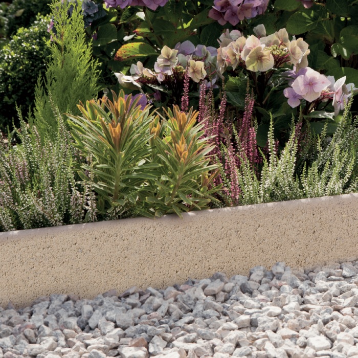 Close-up of buff round top path edging with a textured finish, bordering vibrant garden flowers and shrubs.