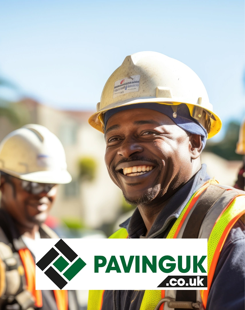 A smiling PavingUK professional in a white hard hat and high-visibility safety vest at a sunny construction site.
